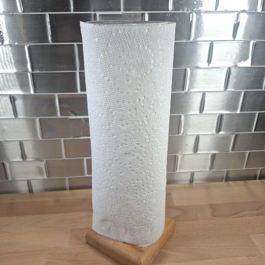 Rouleau d'essuie-tout dressé sur son socle de bois, devant un dosseret de cuisine.