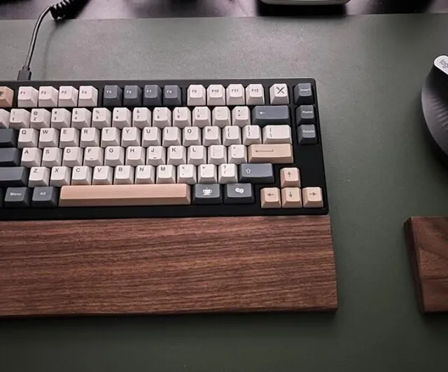 Repose-poignet en noyer placé devant un clavier mécanique, sur un tapis de bureau.